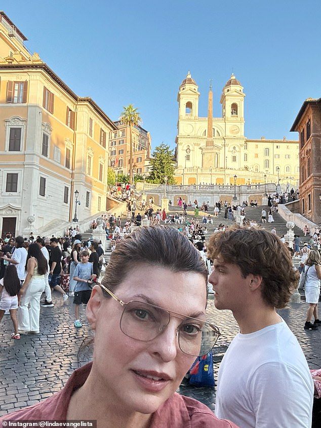 Linda looked chic in a brown button-up shirt with aviator prescription glasses and her dark hair worn back. Augustin smiled for the camera as he had on a white T-shirt with his hair worn wild