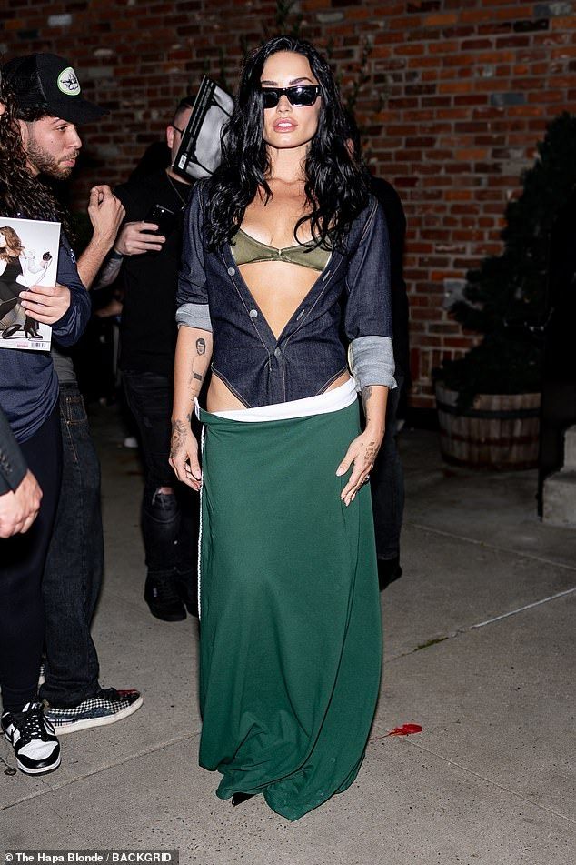 The former Disney child star looked ready to party as she flashed a shiny olive green bra, which she appeared to almost be falling out of, worn under a blue denim topstitched leotard