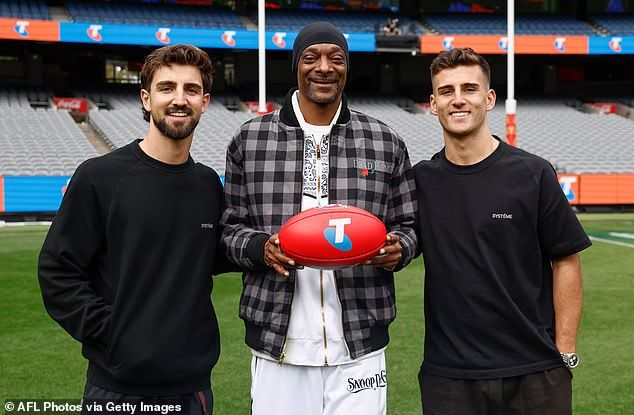 The rapper (centre) touched down in Melbourne on Tuesday, meeting up with AFL brothers Nick (left) and Josh Daicos (right) for a kickabout at the MCG